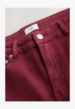 Burgundowe skinny jeans z wysokim stanem, srebrnym guzem i kontrastowym przeszyciem. Gładka tekstura z delikatnym blaskiem.