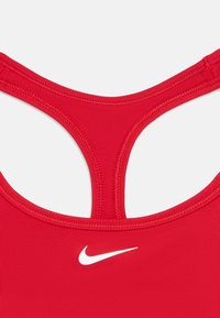 Podroben pogled na hrbtni del rdečega športnega modrčka z zasnovo racerback in belim Nike swoosh logotipom na tkanini.