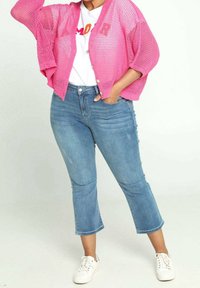 Rosa nätcardigan över en vit t-shirt med grafik, i kombination med ljusblå cropped jeans och vita sneakers. Cardiganen har stora ärmar och knappar.