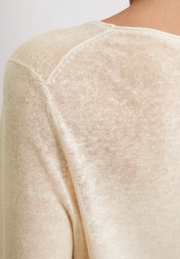 Jasnobeżowy sweter z dzianiny o luźnym, teksturowanym wzorze, z szerokim dekoltem i lekko opuszczonymi szwami na ramionach.