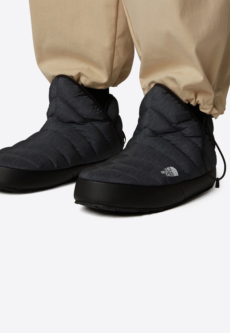 Svarta isolerade slip-on stövlar med quiltat tyg och tjock sula, bärs tillsammans med beige uppvikta byxor, med The North Face-logotyp på sidan.