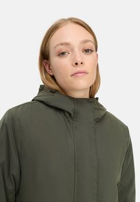 Olivengrøn isoleret jakke med høj krave, hætte og subtil tekstur. Har en fuld frontlynlås og stikninger som accent.