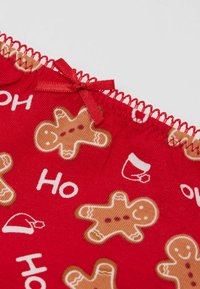 Tessuto rosso con motivi ripetuti di omini di pan di zenzero, testo bianco "Ho" e icone di tazze di caffè. Rifinito con cuciture decorative rosse e nastro.