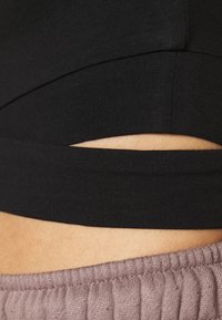 Zbliżenie na środkową część ciała, pokazujące czarny krótki top z małym wycięciem na skórze powyżej ściągacza fioletowych spodni w odcieniu mauve.