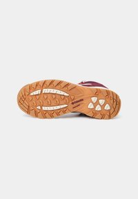 Semelle en caoutchouc marron à crampons d'une chaussure de randonnée violette, montrant des motifs d'adhérence texturés et le logo "Columbia" sur la semelle.