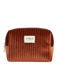 Pochette cosmetica in velluto arancione ruggine con texture a righe verticali. Presenta un'etichetta bianca con la scritta "FABLE ENGLAND" e una zip dorata.