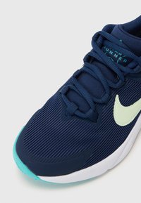 Baskets de sport bleu marine avec tige en tissu texturé, logo vert clair en accent et semelle bleu canard. Comprend des lacets plats et un col rembourré pour plus de confort.