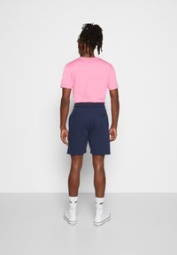 Růžová košile s krátkým rukávem a tmavě modré šortky vyrobené z měkké tkaniny. Šortky mají měkký pás a jednu zadní kapsu.