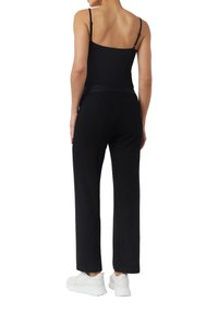 Czarne, luźne spodnie o splocie w jodełkę, zestawione z czarną bluzką na ramiączkach i białymi butami sportowymi.