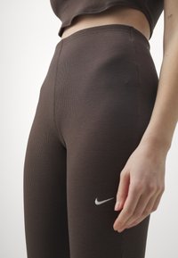 Brown ribbed leggings with a high waist and a subtle Nike logo in white. They feature a smooth texture and fitted silhouette.