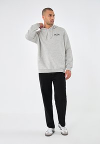 Grå hettegenser med frontlomme, med teksten "NEW YORK". Kombinert med svarte bukser og hvite sneakers, på en ensfarget bakgrunn.