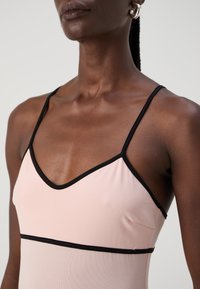 Rochie roz deschis cu accente negre, cu bretele subțiri, decolteu în V și material neted, elastic. Accent pe zona pieptului și umerilor.