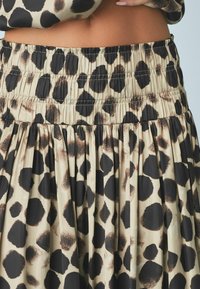 Jupe au motif léopard avec une taille froncée, en tissu fluide, dans des tons beiges et noirs, ornée de taches noires et brunes de différentes tailles.