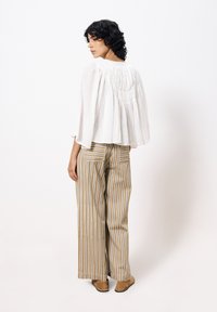 Weiße, strukturierte Bluse mit weiten �Ärmeln und gerafftem Rückendetail, kombiniert mit hochtaillierten, beigen und weißen gestreiften weiten Hosen.