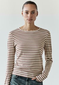 Gestreiftes Langarmshirt in Braun und Creme, mit rundem Ausschnitt und weicher Textur. Kombiniert mit Jeans.