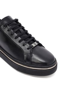 Sneaker in pelle nera con finitura testurizzata, lacci neri piatti, componenti in metallo argentato e suola in gomma a contrasto con un design sottile.