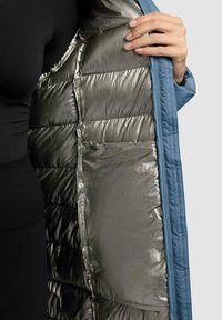 Sininen ulkotakki, jossa on hopeanvärinen metallinhohtoinen vuoraus. Takissa näkyvä tikkikuvio ja sisäinen taskudetaili.