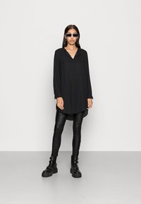 Black long-sleeve shirt with a pointed collar, paired with fitted black leather leggings and chunky black boots. Features minimalistic design.