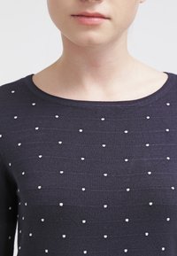 Granatowy sweter z okrągłym dekoltem, z białymi kropkami równomiernie rozmieszczonymi na fakturowanym materiale.