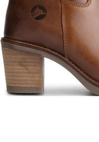 Bruine leren enkelboot met een gestapelde beige hak. Bevat een gestructureerd oppervlak en een geëtst logo nabij de bovenkant. Naaddetails zijn zichtbaar.