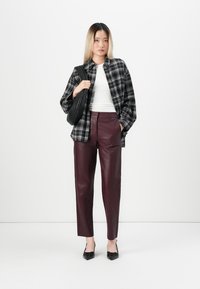 Zwart-wit geruite oversized blouse, witte aansluitende blouse, bordeaux leren broek, zwarte schoudertas, zwarte hakken, neutrale achtergrond.