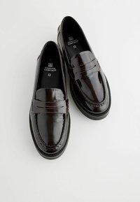 Mocassins en cuir verni noir avec une finition lisse, présentant une bande à pièce, des détails de couture et une semelle en caoutchouc basse.