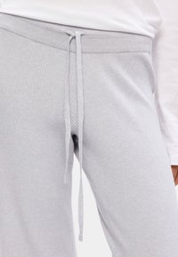 Calças de treino de malha ribada cinza claro com um cós elástico ajustável. A textura do tecido é suave, apresentando um design simples sem padrões ou acentos adicionais.