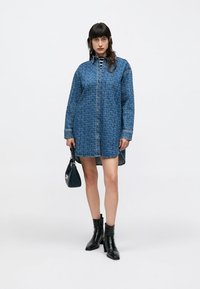 Sininen farkkumekko, jossa on teksturoitu kuvio, nappisuljenta ja pitkät hihat. Yhdistetty mustiin nilkkureihin ja pieneen mustaan kävelykassiin.