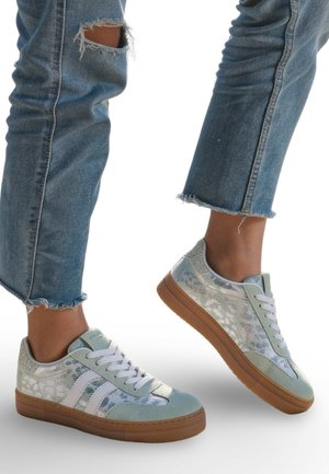 Pieds portant des baskets bleu clair avec des lacets blancs et des semelles en caoutchouc, assorties à un jean bleu raccourci avec des ourlets effilochés.