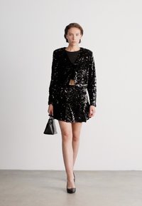 Svart, paljettbeströdd kort jacka och matchande utsvängd kjol, kombinerad med en figurnära topp och svarta klackar. Accessoarer: en liten svart handväska.