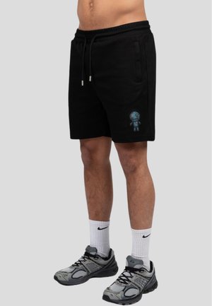 Shorts in cotone neri con elastico in vita, tasche laterali e un dettaglio ricamato blu su la gamba sinistra. Abbinati a scarpe da ginnastica grigie.
