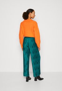 Suéter naranja de punto trenzado combinado con pantalones anchos a rayas en tonos teal y botines negro de tacón cuadrado.