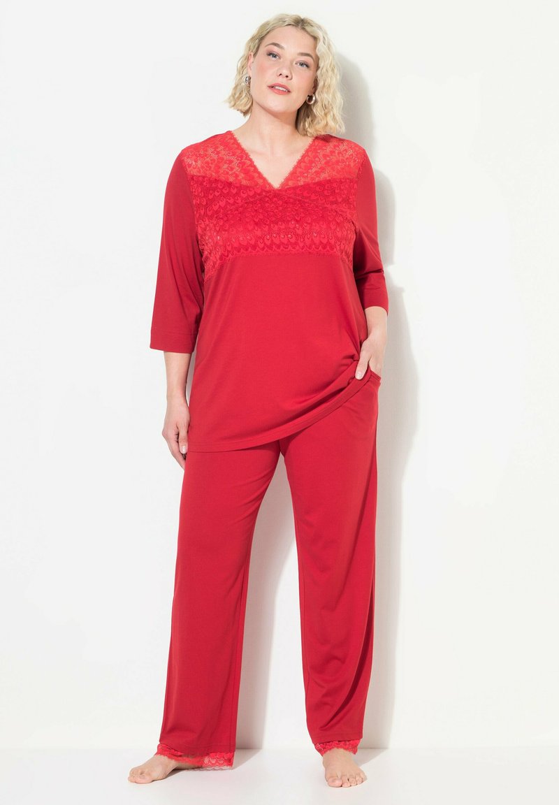 Rød loungewear-sæt med en V-hals trøje med blondeaccent og løstsiddende bukser med blondekant ved kanten. Blødt stof, afslappet pasform.