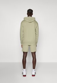Lichtgroene hoodie met een achterhoed, gecombineerd met bijpassende shorts. De stof lijkt zacht, met ribgebreide manchetten en een ontspannen pasvorm.
