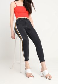 Svarta högmidjade jeans med vita och gula sidostripes, kombinerat med en röd crop top och vita blockklack-sandaler.