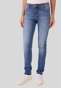 Schlankes Jeans im hellblauen Denim, mit fünf Taschen, einem Reißverschluss und Knopf, sowie einem ausgewaschenen Finish. Kombiniert mit weißen Sneakers.