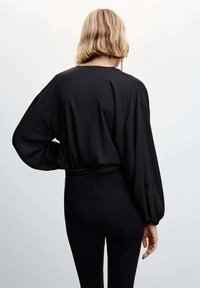 Blouse noire avec manches longues et amples et taille cintrée, en tissu doux, vue de dos. Design simple et élégant.