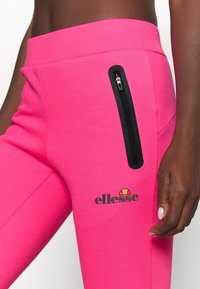 Roze joggingbroek van zachte stof, met een zwarte ritszak aan de zijkant en een gedrukt logo. Geribbelde tailleband maakt het ontwerp af.