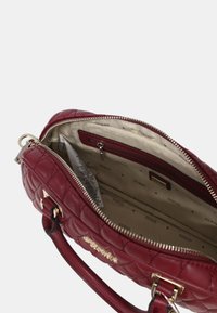 Bolso burdeos acolchado con herrajes en tono dorado y cierre de cremallera. Interior forrado con un patrón de logo, que incluye un bolsillo con cremallera y espacio de organización.