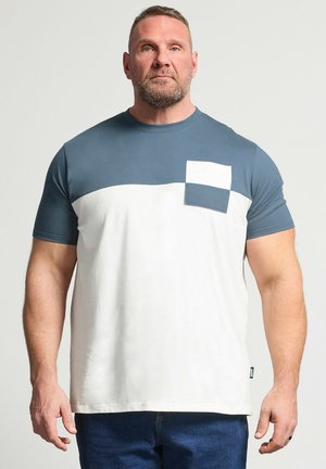 Muskelbepackter Mann trägt ein kurzärmliges T-Shirt mit Farbblock-Design, blauem oberen und weißem unteren Teil sowie einer quadratischen Brusttasche.