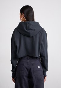 Cropped hoodie in dark grey fabric with a hood; features dropped shoulders and raw hem, paired with dark baggy pants with patch pockets.