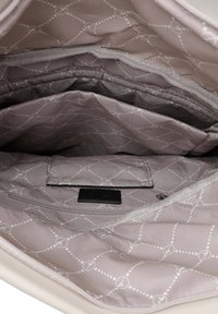Interior de bolsa beige con tres compartimentos, forrado en una tela marrón claro con un patrón de diamantes y un pequeño bolsillo con cremallera.