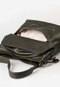 Borsa a spalla in pelle verde scuro con pattina e bottoni magnetici, parzialmente aperta che mostra l'interno foderato in tessuto beige a motivo.