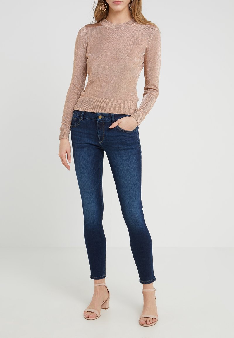 Ljusrosa, strukturerad långärmad topp med en åtsittande silhuett, kombinerad med mörkblå skinny jeans och beige klacksandaler.