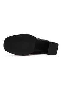 Semelle de chaussure habillée noire avec semelle inférieure en caoutchouc texturé et talon carré, vue par en dessous sur fond blanc.