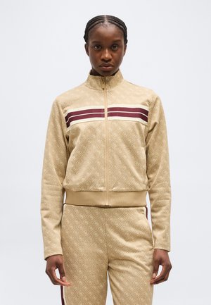 Person wearing beige patterned zip-up jacket and matching pants with maroon and white stripes across the chest and down the sides.