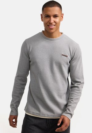 Camisa gris de manga larga con una superficie texturada y acanalada. Presenta un escote redondo y una marca sutil en el pecho. Se lleva con pantalones oscuros.