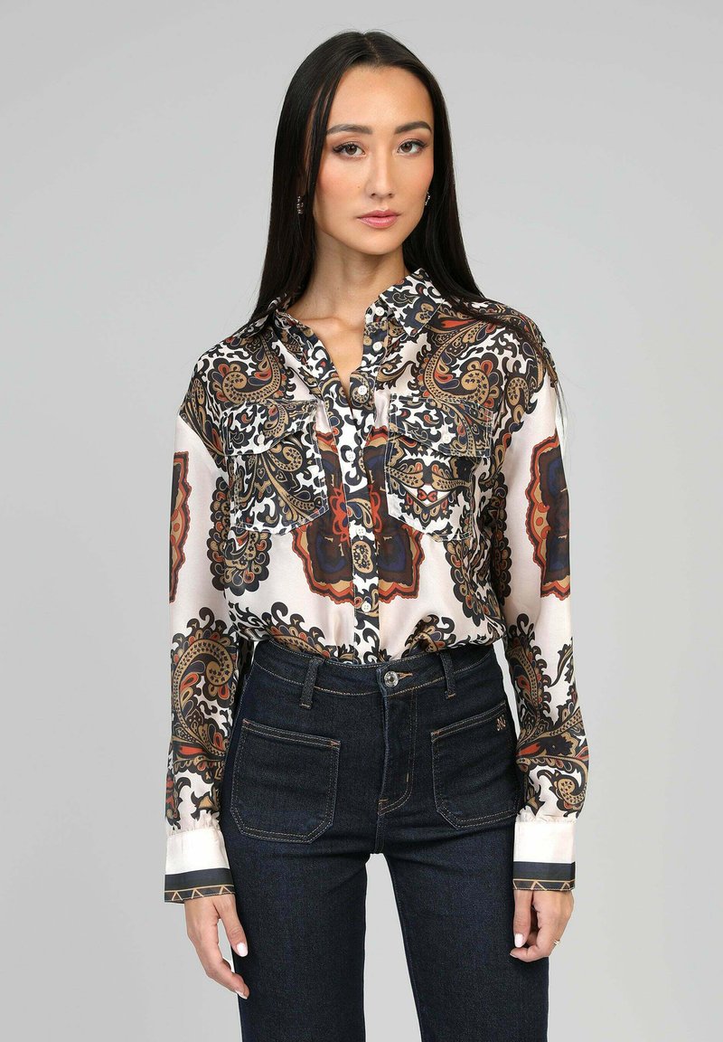 Blouse en satin avec un motif cachemire noir, orange et crème. Présente un devant boutonné, deux poches poitrine et des poignets contrastants.