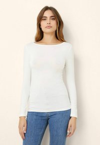 Langärmliges weißes Oberteil mit einem runden Ausschnitt, aus glattem Stoff, kombiniert mit blauen Jeans. Figurbetontes Design mit minimalen Details.