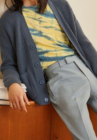 Överdimensionerad marinblå cardigan med texturerad stickning, fem knappar, kombinerad med en gul och blå tie-dye skjorta samt ljusgrå skräddarsydda byxor.